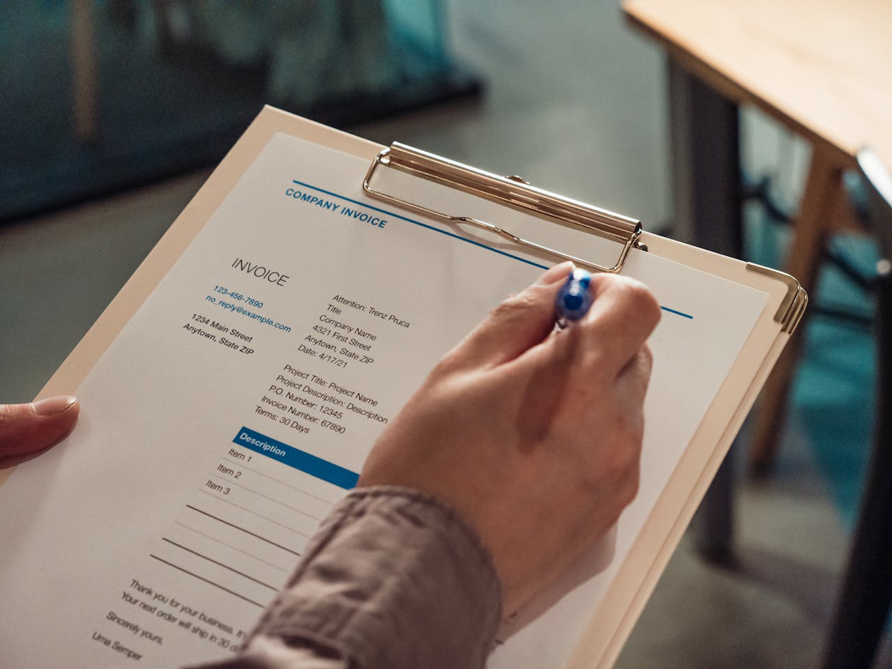 creative Person's hand holding a company invoice on a clipboard with a pen.