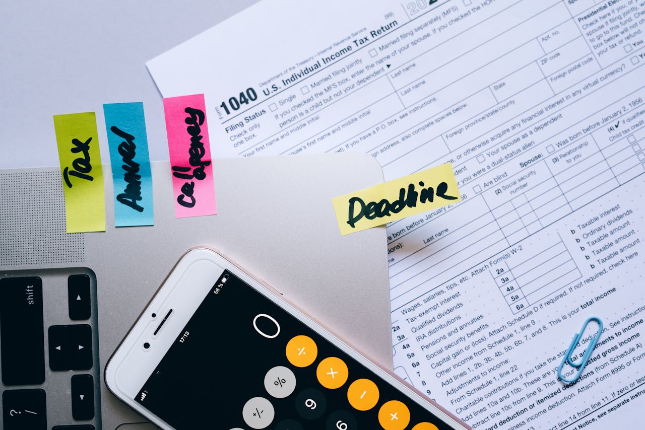 Services-01 Office desk flat lay showing tax documents, calculator app on smartphone, sticky notes, and paperclips.